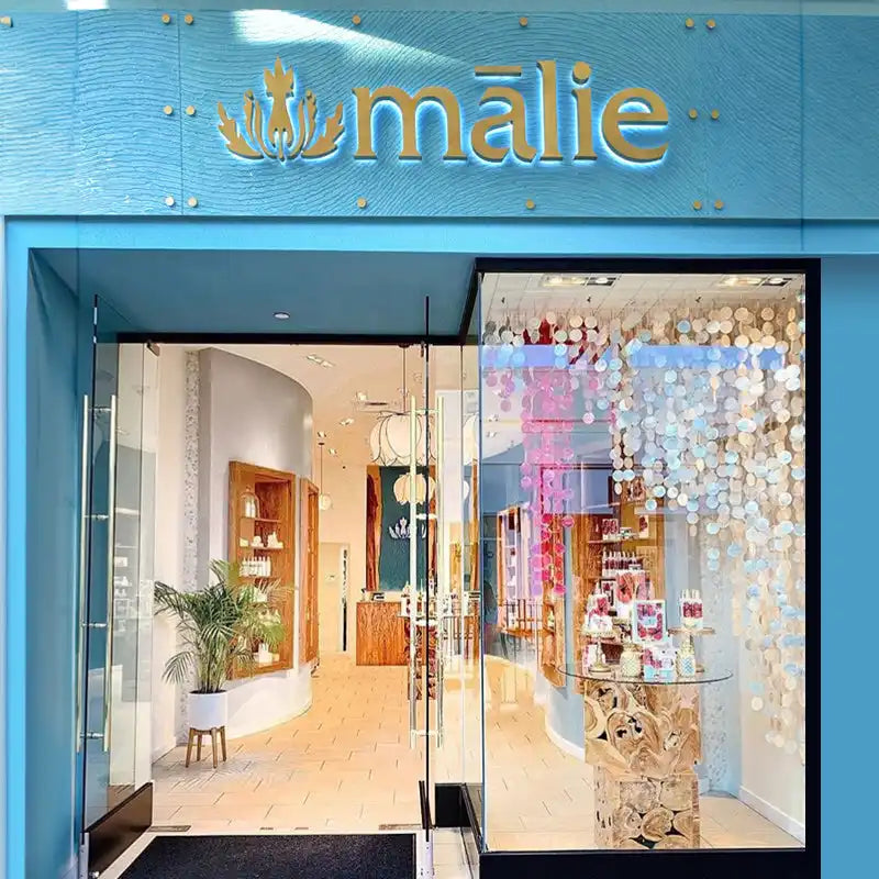 Turquoise-framed storefront of a boutique called ’Malie’ with glass doors and decorative window displays.